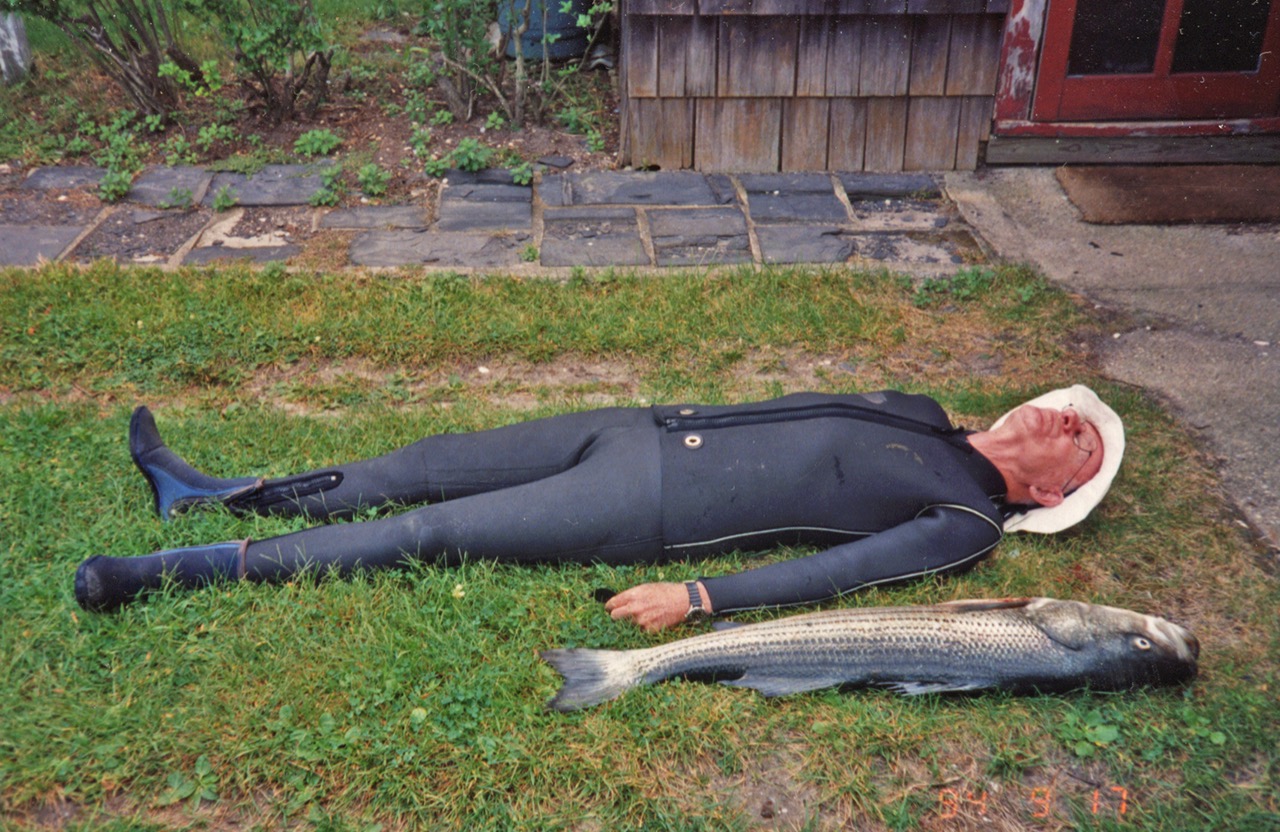Dennis Flanagan in a wet suit, lying on the lawn next to the striped bass he just speared in Great South Bay.